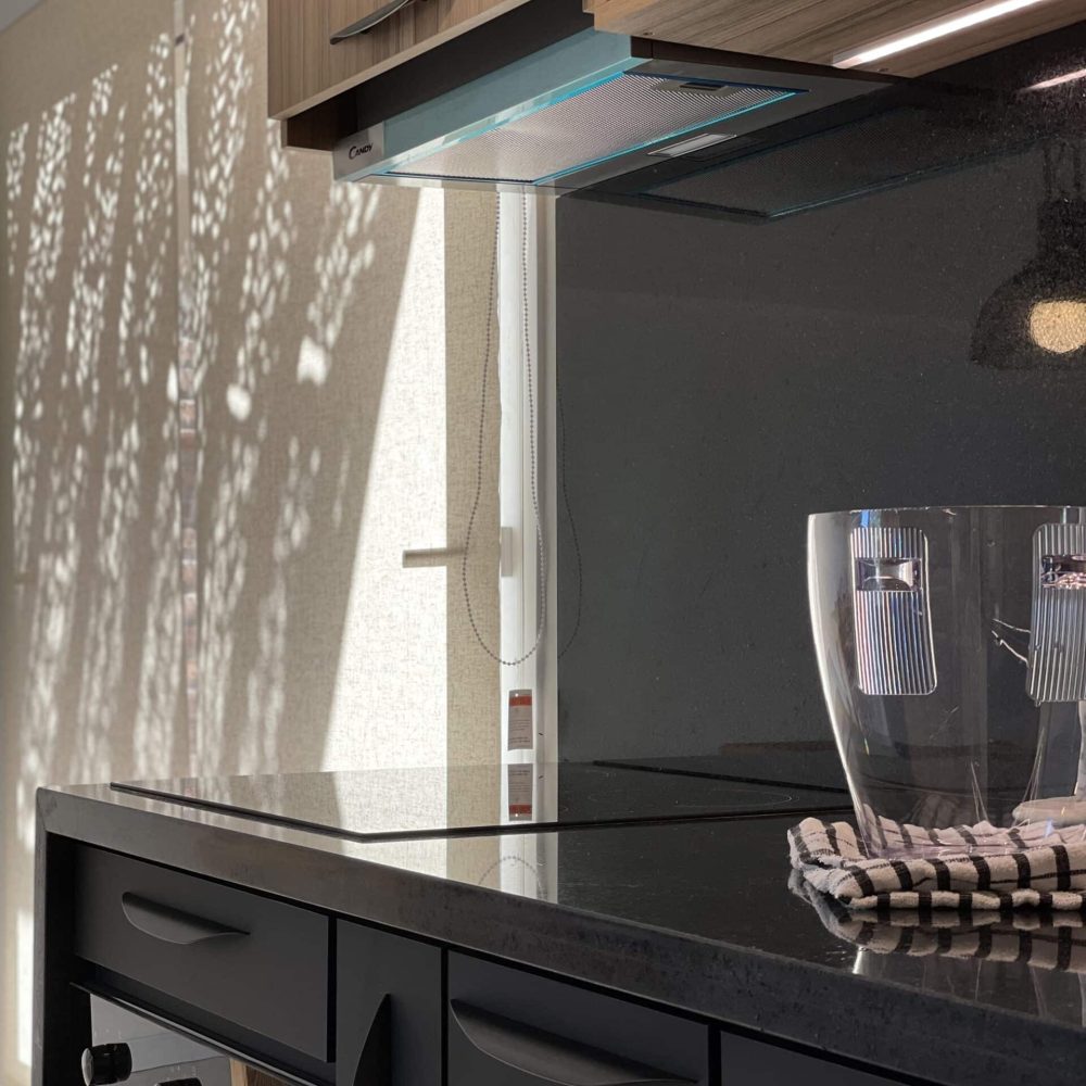 Proyecto de diseño de cocina en Haras del Lago, un barrio cerrado en Canelones, Uruguay. La cocina presenta muebles en acabado maderado, un tablero negro antihuella y mesadas de granito negro absoluto, combinando elegancia y funcionalidad.