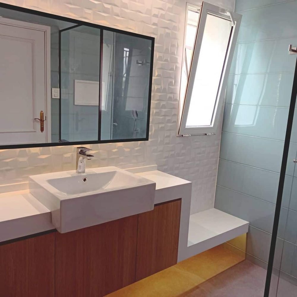 Baño contemporáneo en el barrio del Prado, Montevideo. Revestimientos en cerámica verde aguamarina, mesada de cuarzo blanco convertida en banco, mueble de roble claro, y cabina de ducha con cristal transparente y perfilería negra. Iluminación ambiental detrás del espejo y mueble flotante para crear un ambiente acogedor y moderno.