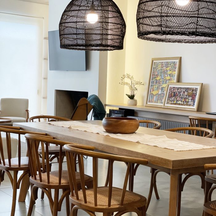 Descubre la elegancia relajada de nuestra sala de estar en esta casa introspectiva con vista a la piscina en la zona de playas de José Ignacio. Este espacio, que incorpora un comedor, se caracteriza por su diseño funcional y acogedor. Un mueble multifuncional de 5 metros sirve como aparador para el comedor y como escritorio, albergando incluso una enfriadora de vinos para añadir un toque de sofisticación. El centro de atención de la sala es un cómodo sofá chaise en forma de L con una funda de tussor, acompañado de una butaca complementaria para mayor comodidad. Las cortinas de lino suavizan la luz natural, creando un ambiente sereno y acogedor perfecto para relajarse y disfrutar de la vista al aire libre.