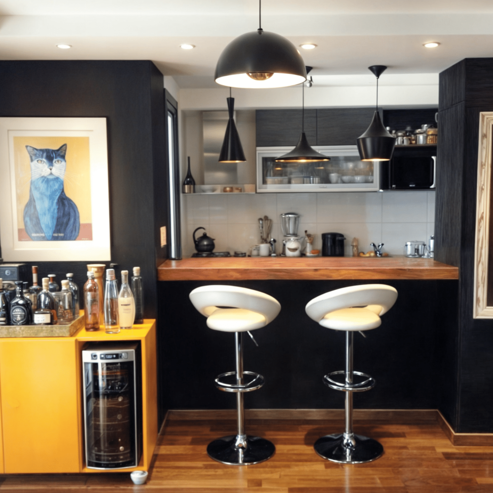 Sala de estar con pared en efecto cemento alisado gris, sofa de cuero negro, mueble barcito amarillo laqueado, barra de madera natural, muros oscuros con cuadro y gatos pintados en tiza, cuadros de izaguirre, parlante de bang and olufsen