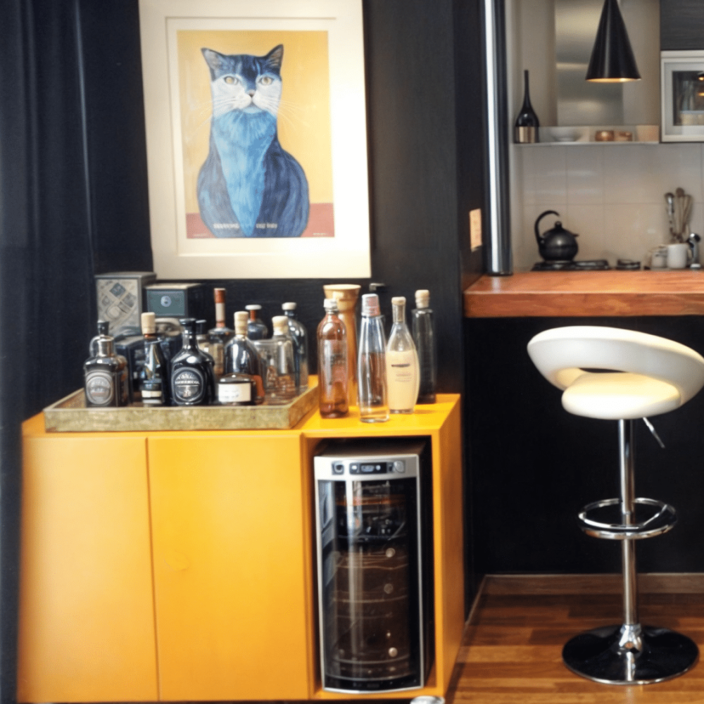 Sala de estar con pared en efecto cemento alisado gris, sofa de cuero negro, mueble barcito amarillo laqueado, barra de madera natural, muros oscuros con cuadro y gatos pintados en tiza, cuadros de izaguirre, parlante de bang and olufsen