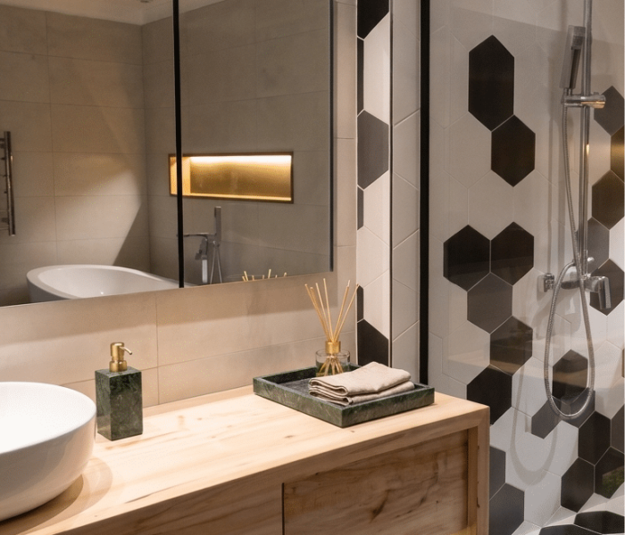 Diseño de baño contemporáneo en Altos de La Tahona, con bañera exenta, ducha vidriada, mueble de madera y revestimiento hexagonal en blanco, gris y negro.